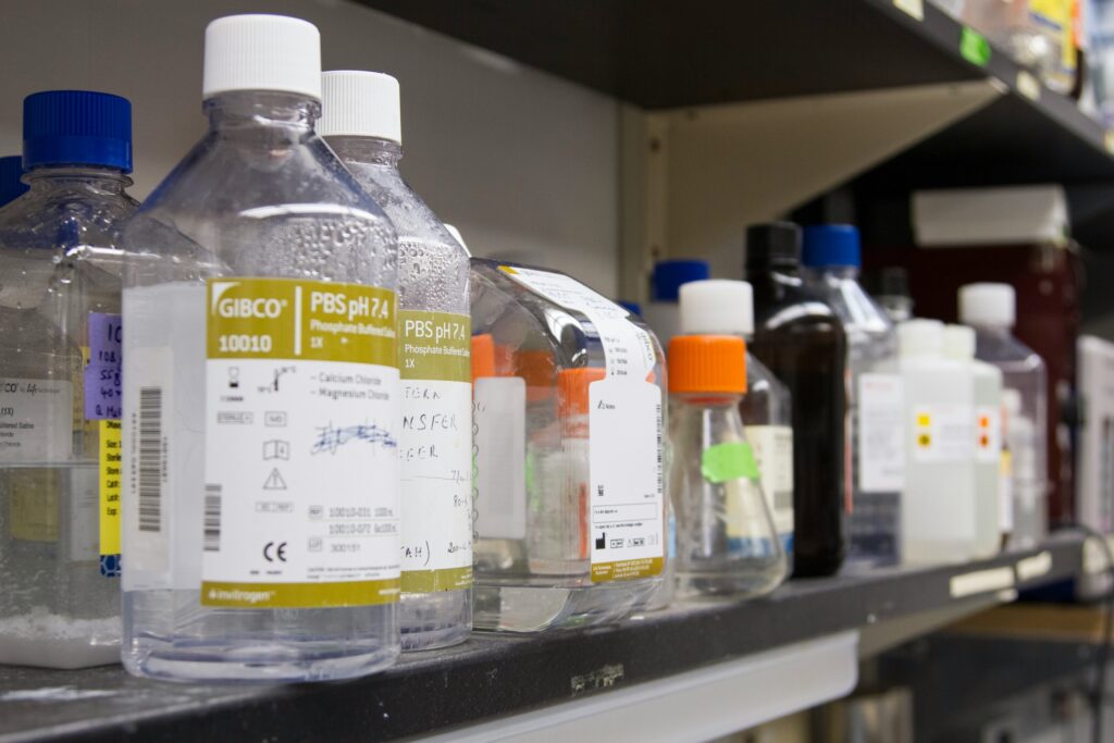 Close-up of chemicals and reagents in HDPE bottles arranged on a shelf in a lab setting.