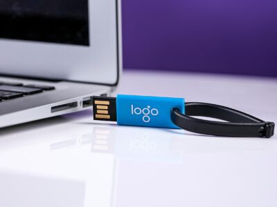 Close-up of a blue USB flash drive with a keyring partially inserted into a silver laptop, symbolizing data storage, transfer, and compliance practices.