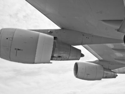 The image shows a close-up, underside view of a large aircraft wing and its engines in black and white. Visible are multiple jet turbines, detailing the nacelles and structural components of the engine mounts. This context highlights the use of ceramics in aerospace engineering, particularly in thermal shielding, engine components, and high-stress zones. Advanced ceramics are commonly utilized here for their high heat resistance, lightweight properties, and durability, which are essential in the demanding environments of aviation and aerospace systems.