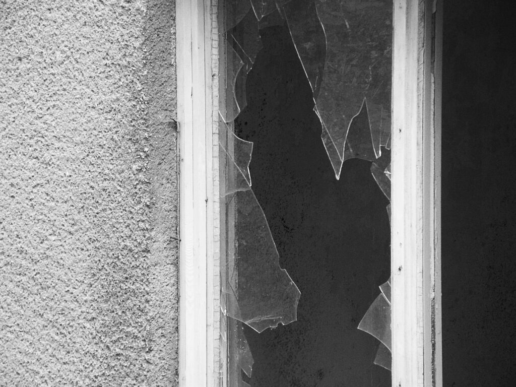 The image shows a broken windowpane with large, jagged shards of glass still in the frame. This kind of scene is often used in forensic analysis to determine the point and direction of impact and the type of force that caused the breakage.
