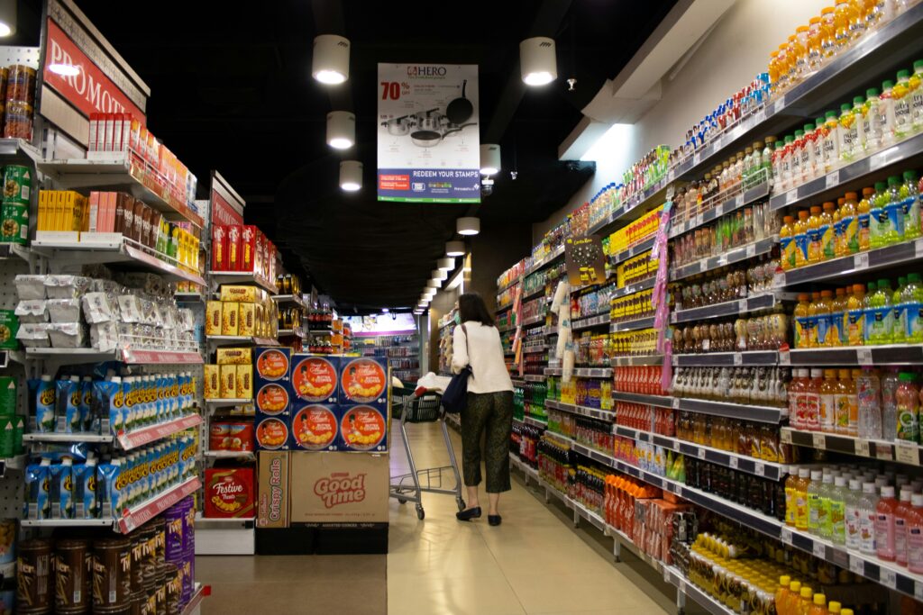 A female shopper walking with a cart along the aisles of a supermarket.