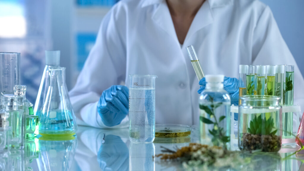 A researcher with gloves works on plant samples in solutions and other glassware in a lab setting.
