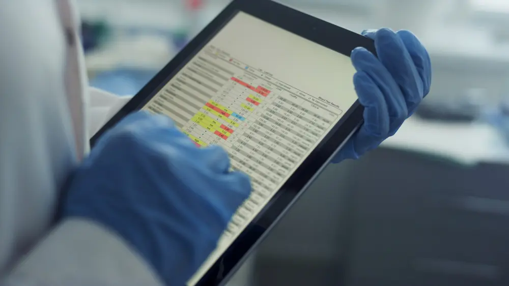 Gloved hands using a tablet, checking health history data in a clinic.