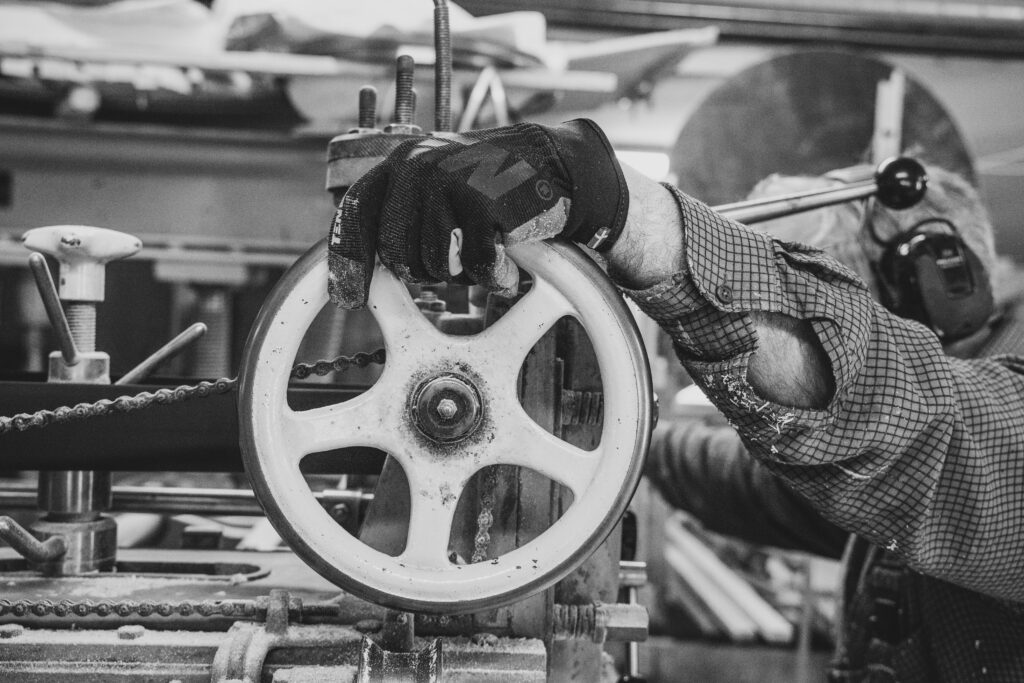 A factory worker controls a pulley wheel of a machine with a gloved hand and PPE.