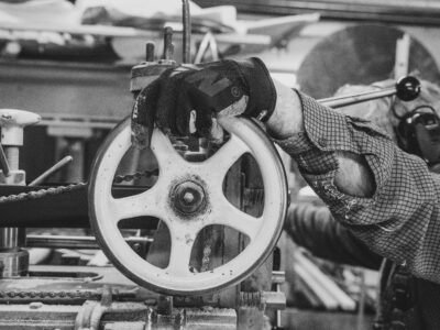 A factory worker controls a pulley wheel of a machine with a gloved hand and PPE.