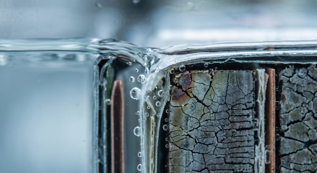 Close-up of water breaching a cracked lithium-ion battery casing, creating bubbles as it contacts internal cell components.