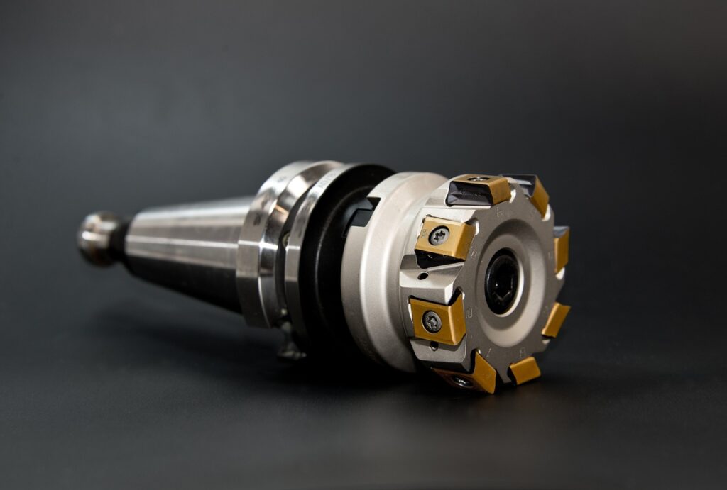 Close-up of a metal milling cutter tool with multiple replaceable carbide inserts, placed on a dark surface.