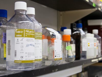Close-up of chemicals and reagents in HDPE bottles arranged on a shelf in a lab setting.
