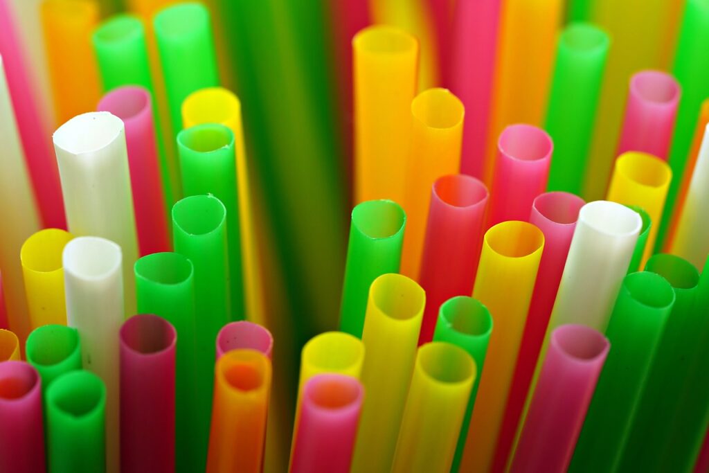 Close-up of colorful plastic drinking straws in shades of green, yellow, pink, orange, and white, arranged vertically.