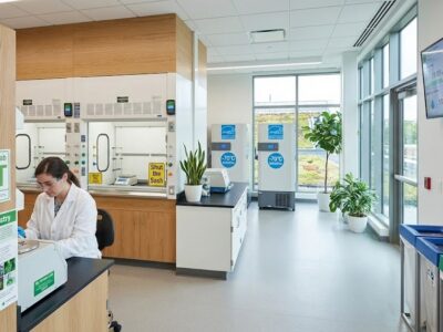 Scientist working in a sustainable laboratory featuring My Green Lab ACT certification signage, recycling stations, and energy-efficient ultra-low temperature freezers set to -70 degrees to reduce energy consumption.